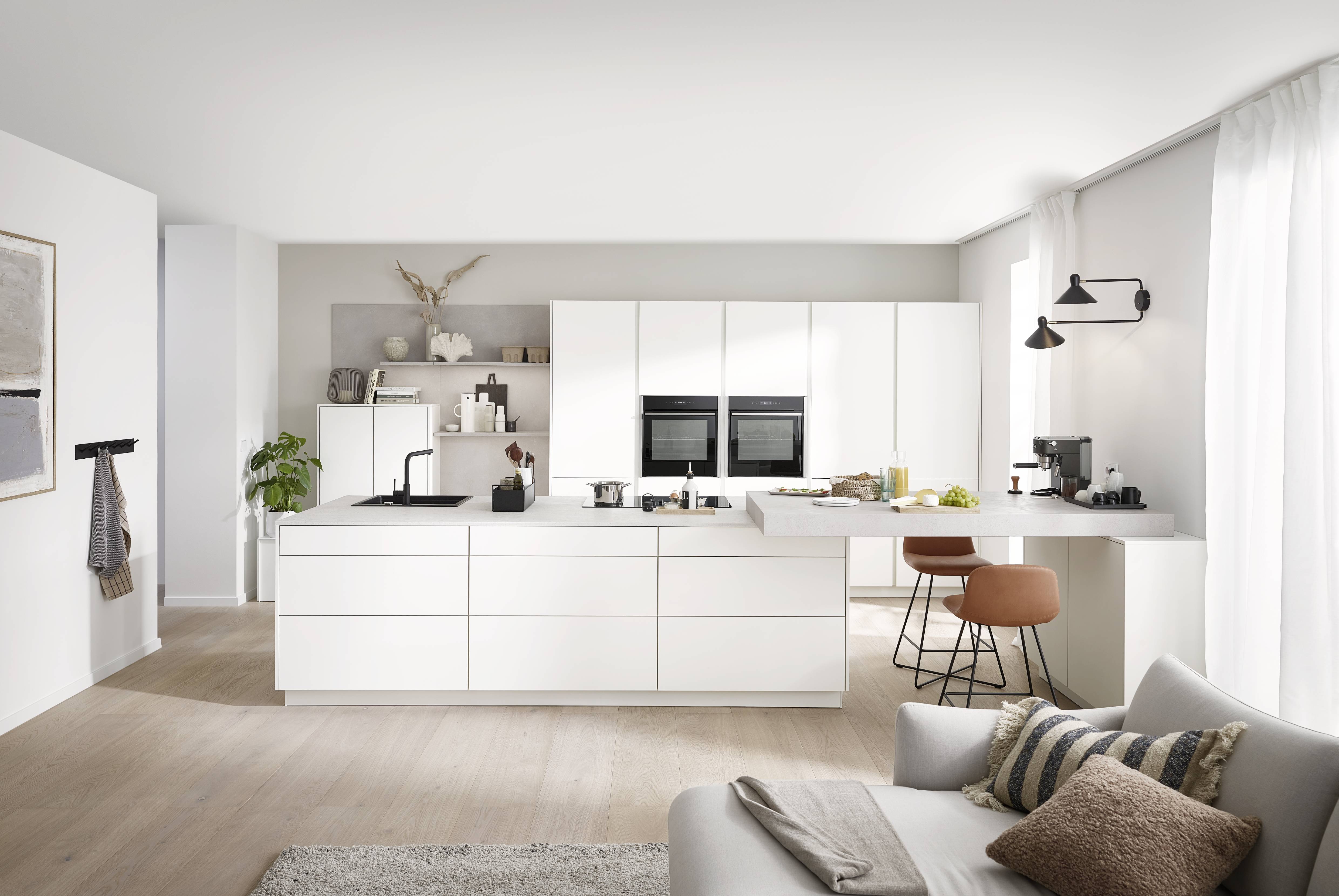 Minimalist white kitchen with an oversized island, integrated appliances, and a clean open-plan living area