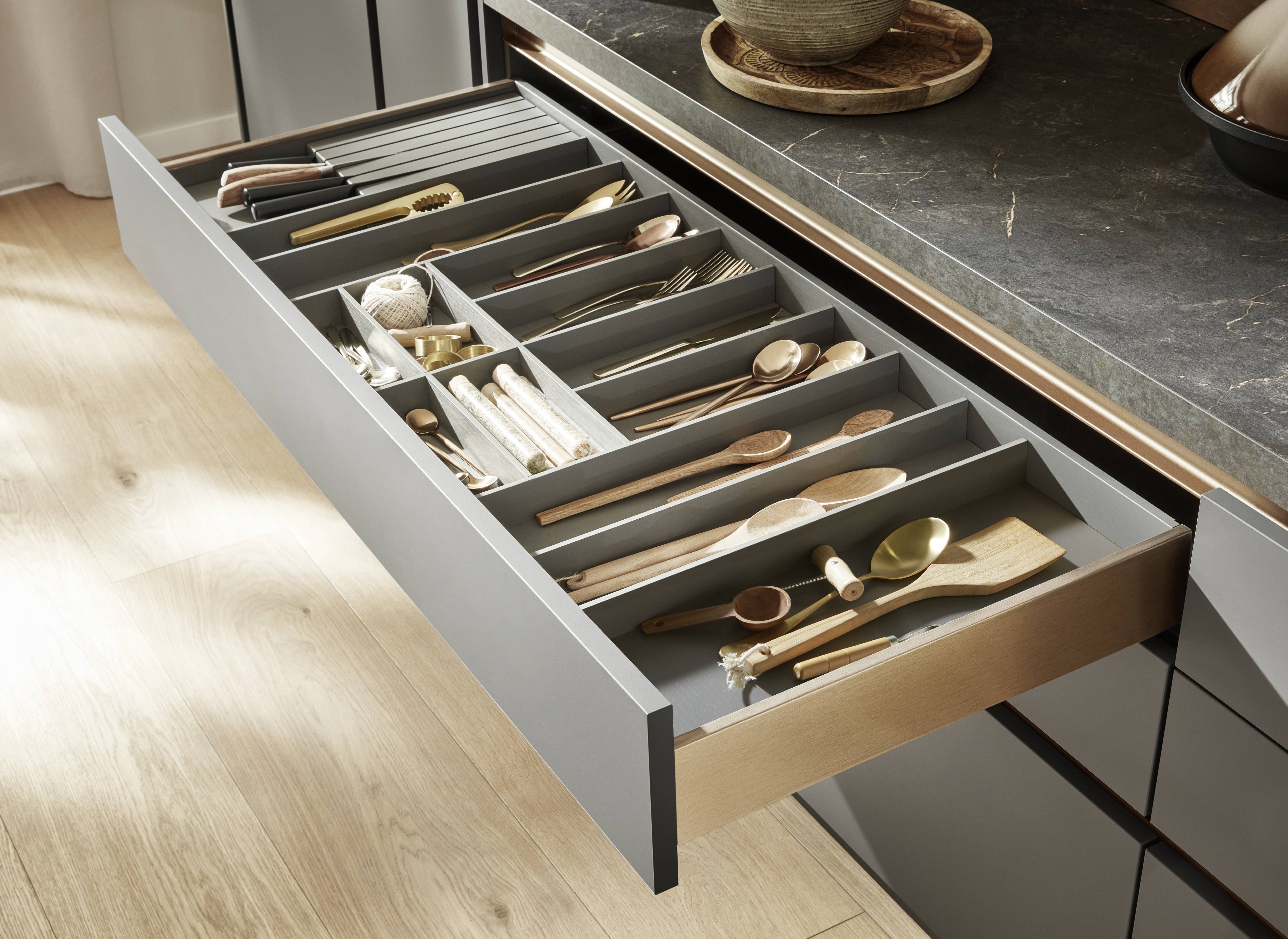 Open kitchen drawer with a modular cutlery organizer neatly separating utensils, knives, and cooking tools beneath a dark stone countertop.