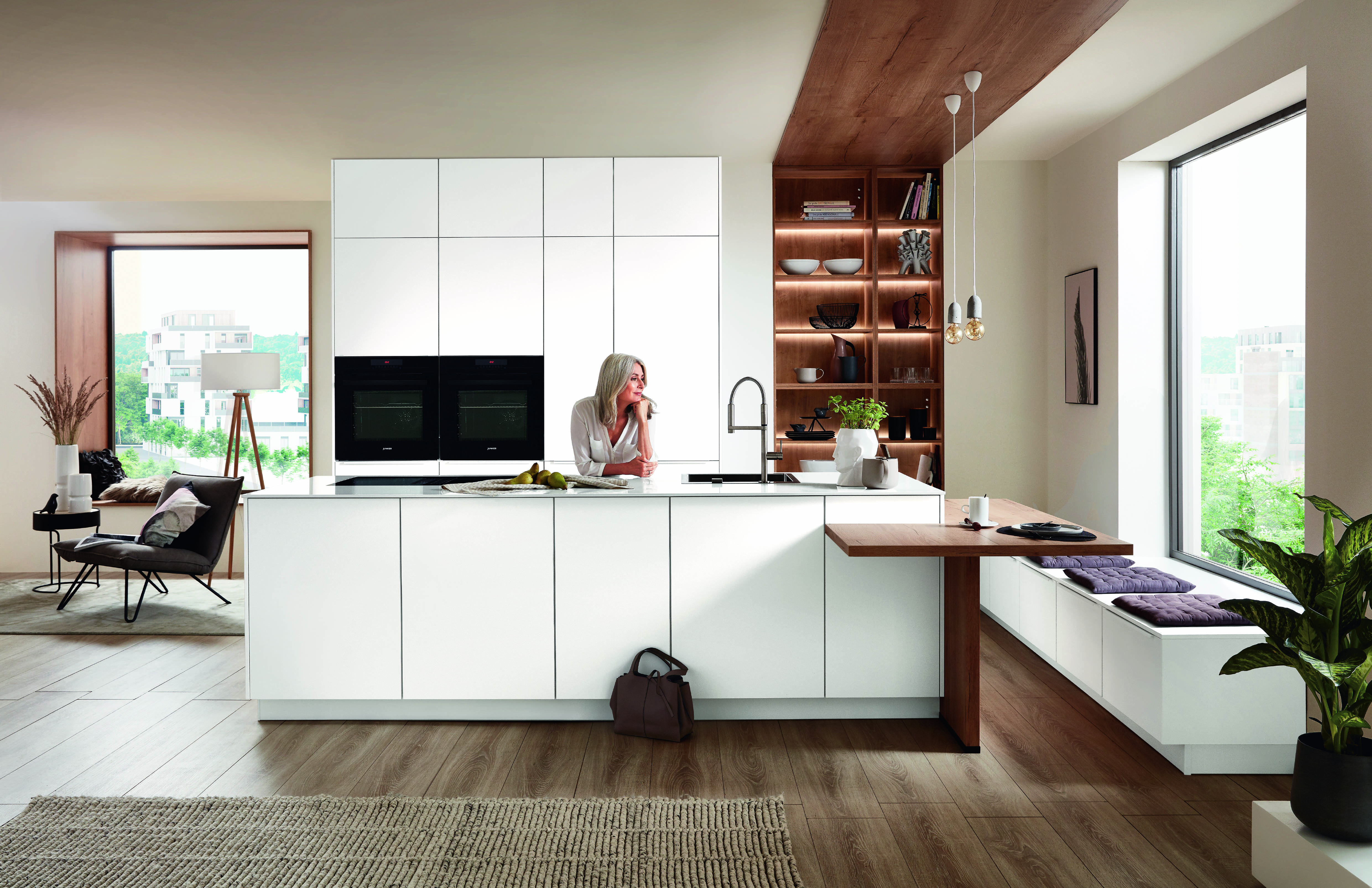 Open plan kitchen with white island and warm wood accents Bright open plan kitchen with a white island, warm wood accents, built-in ovens, and casual seating by the window