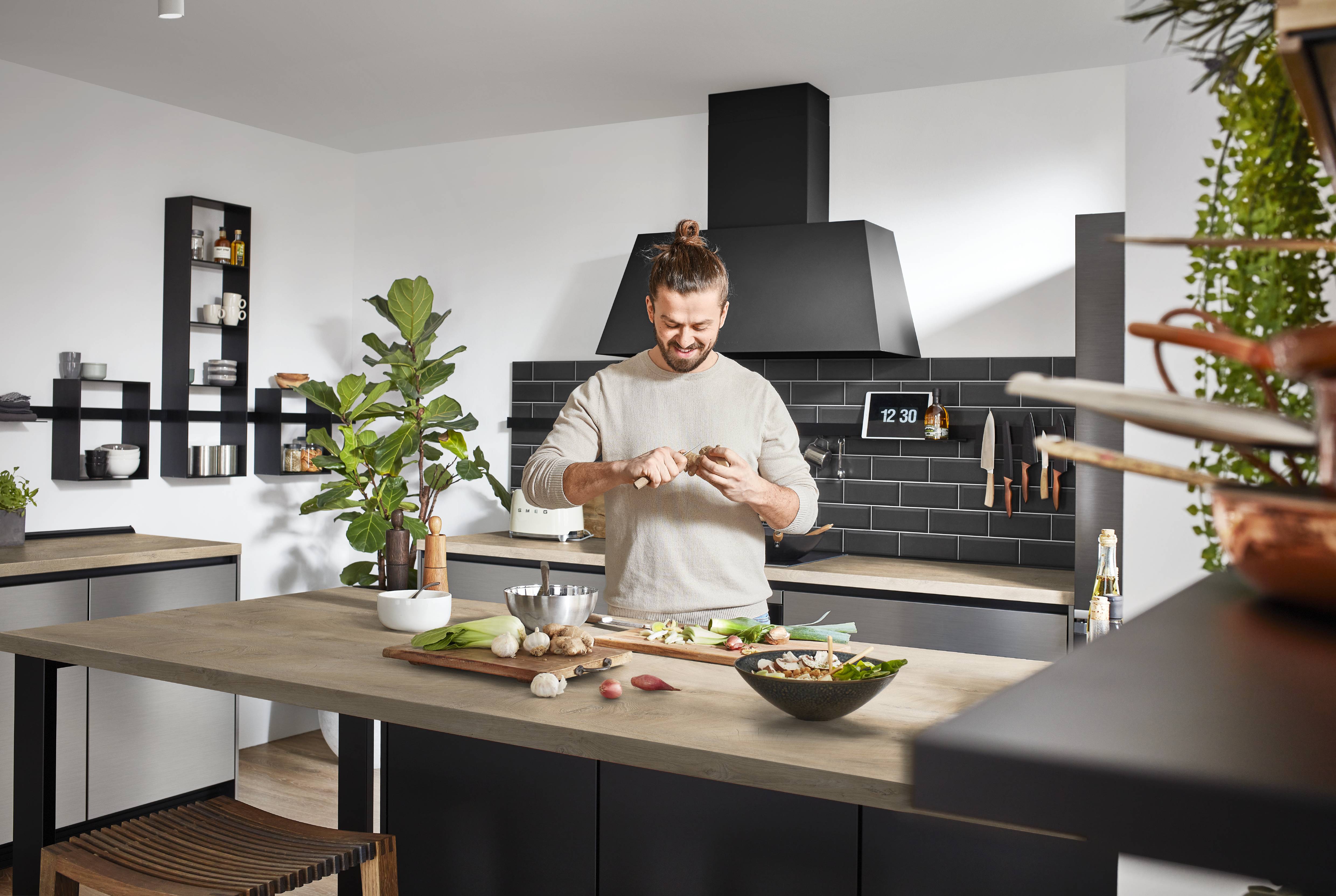 Modern Kitchen Lifestyle Scene with Spacious Island Person preparing food in a modern black-and-wood kitchen with a large island, open shelving, matte black range hood, and subway tile backsplash.