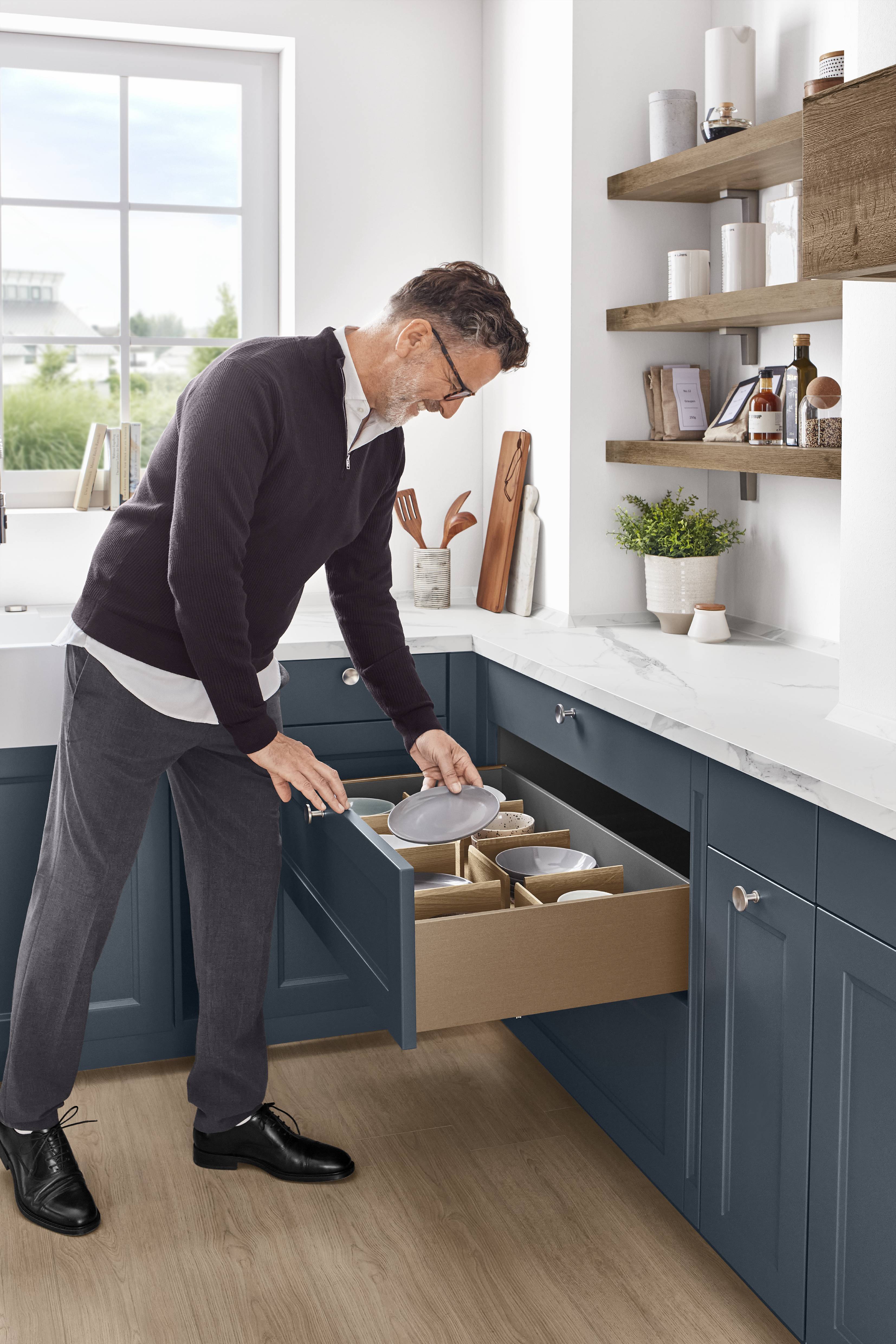 Homeowner organizing dishware in a wide drawer within a blue custom kitchen, highlighting a calm and comfortable everyday workflow