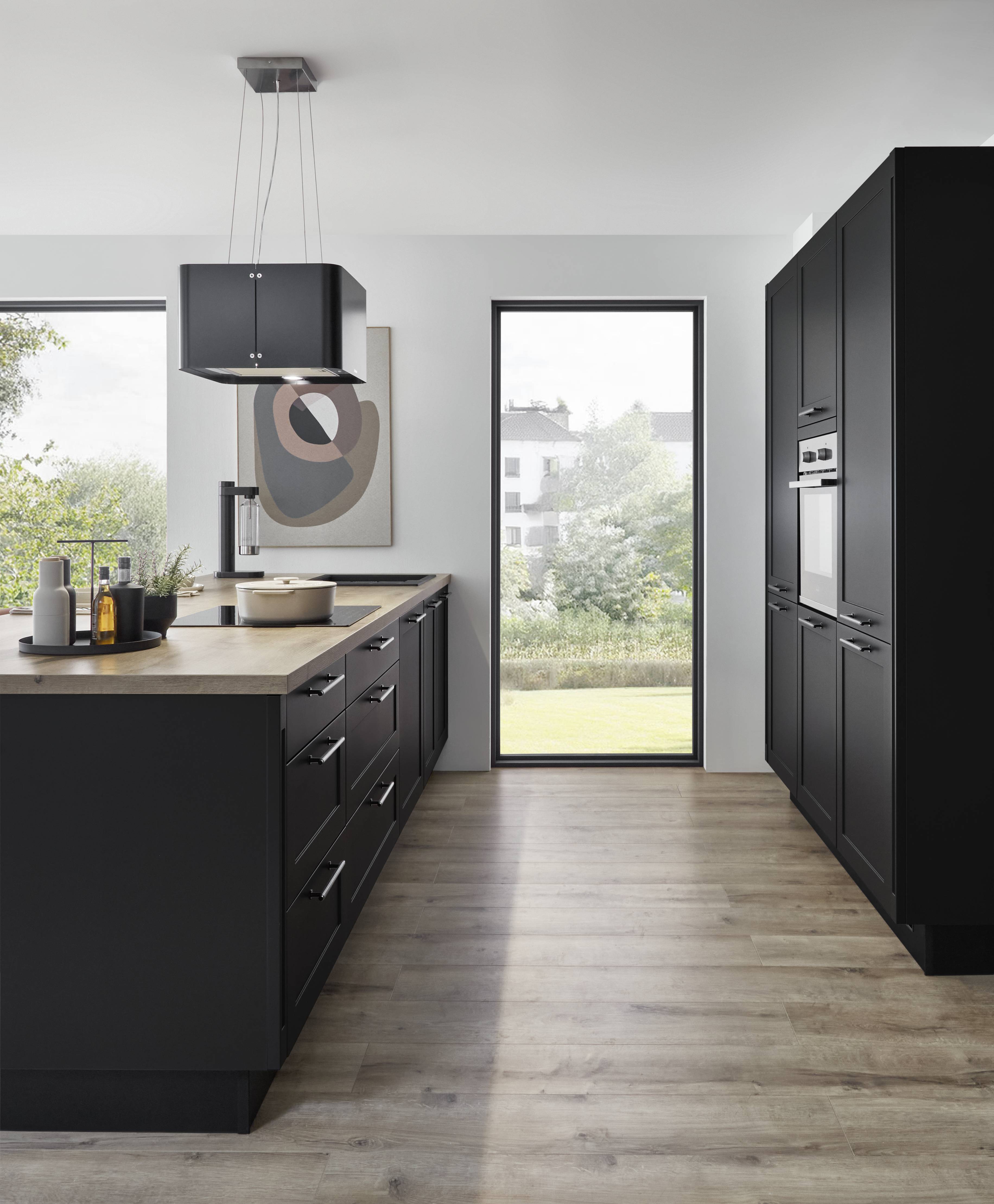 Modern German kitchen featuring sleek black cabinetry, a spacious island with a wood countertop, integrated appliances, pendant lighting, and large windows overlooking a garden.