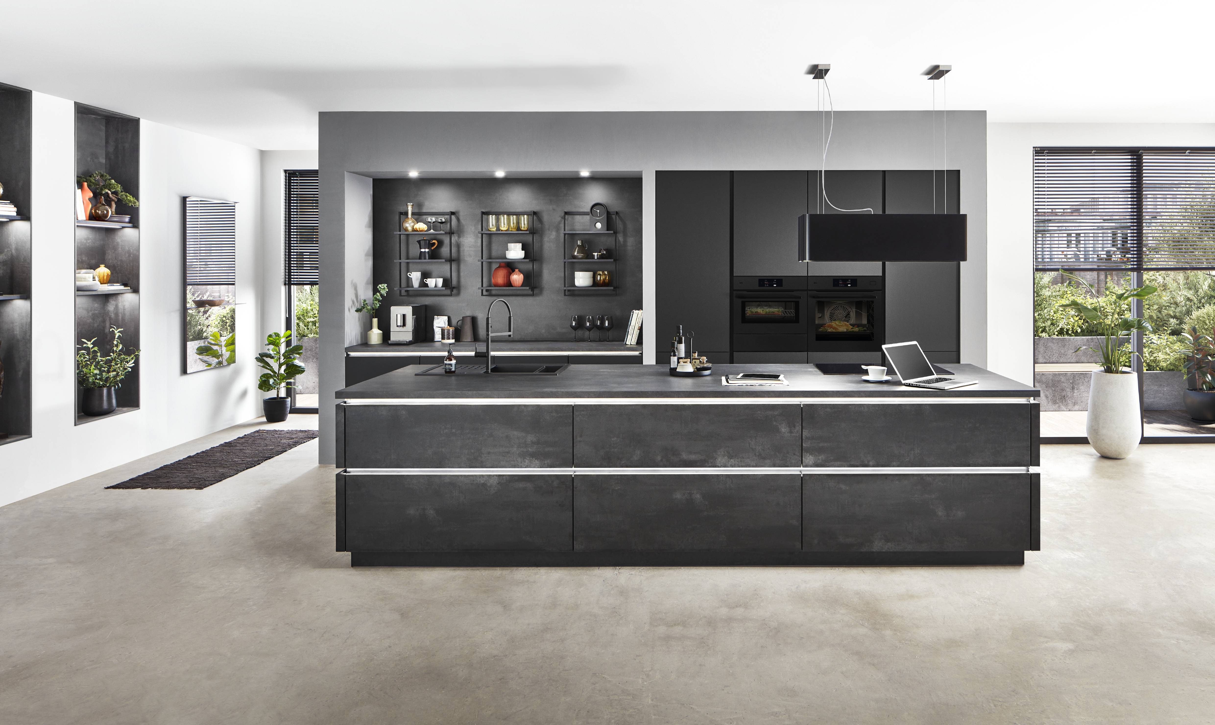 A sophisticated modern German kitchen featuring dark cabinetry, layered lighting, integrated appliances, open shelving, and a spacious island designed for both everyday living and entertaining.
