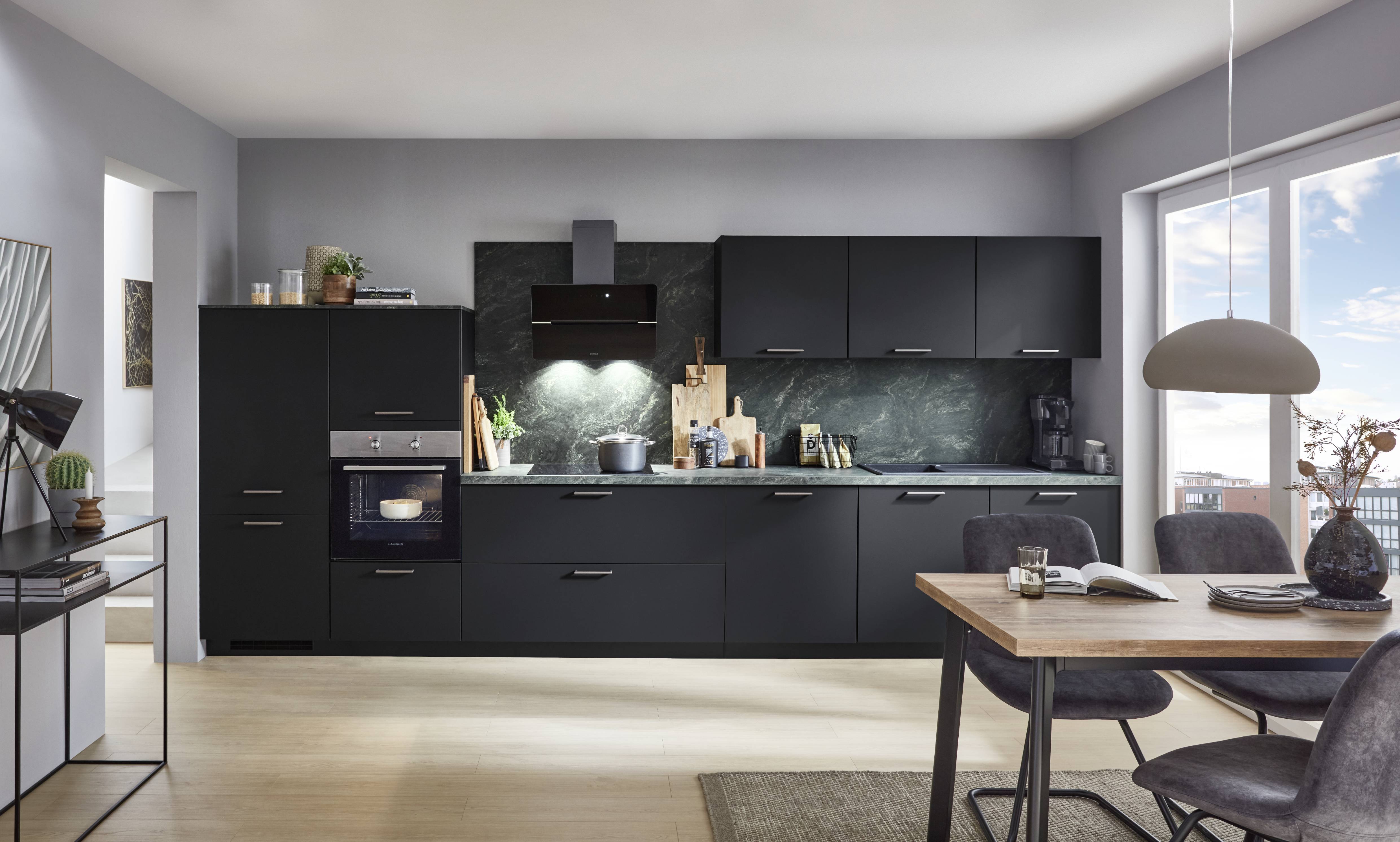 Modern black kitchen with sleek cabinets, marble backsplash, built-in appliances, and a wooden dining table by large windows.