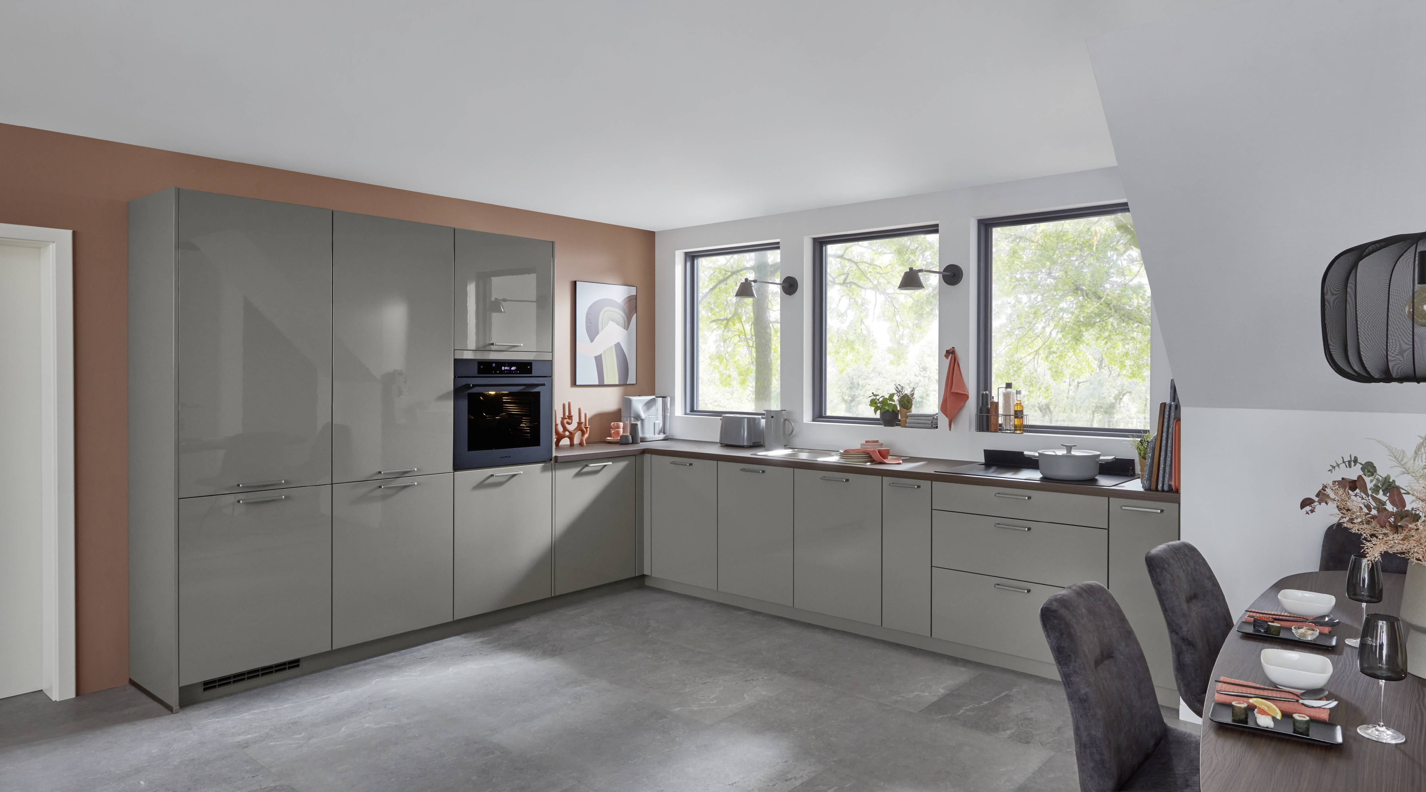 A sophisticated German kitchen featuring sleek gray cabinetry, integrated appliances, warm wood accents, and expansive windows that fill the space with natural light.