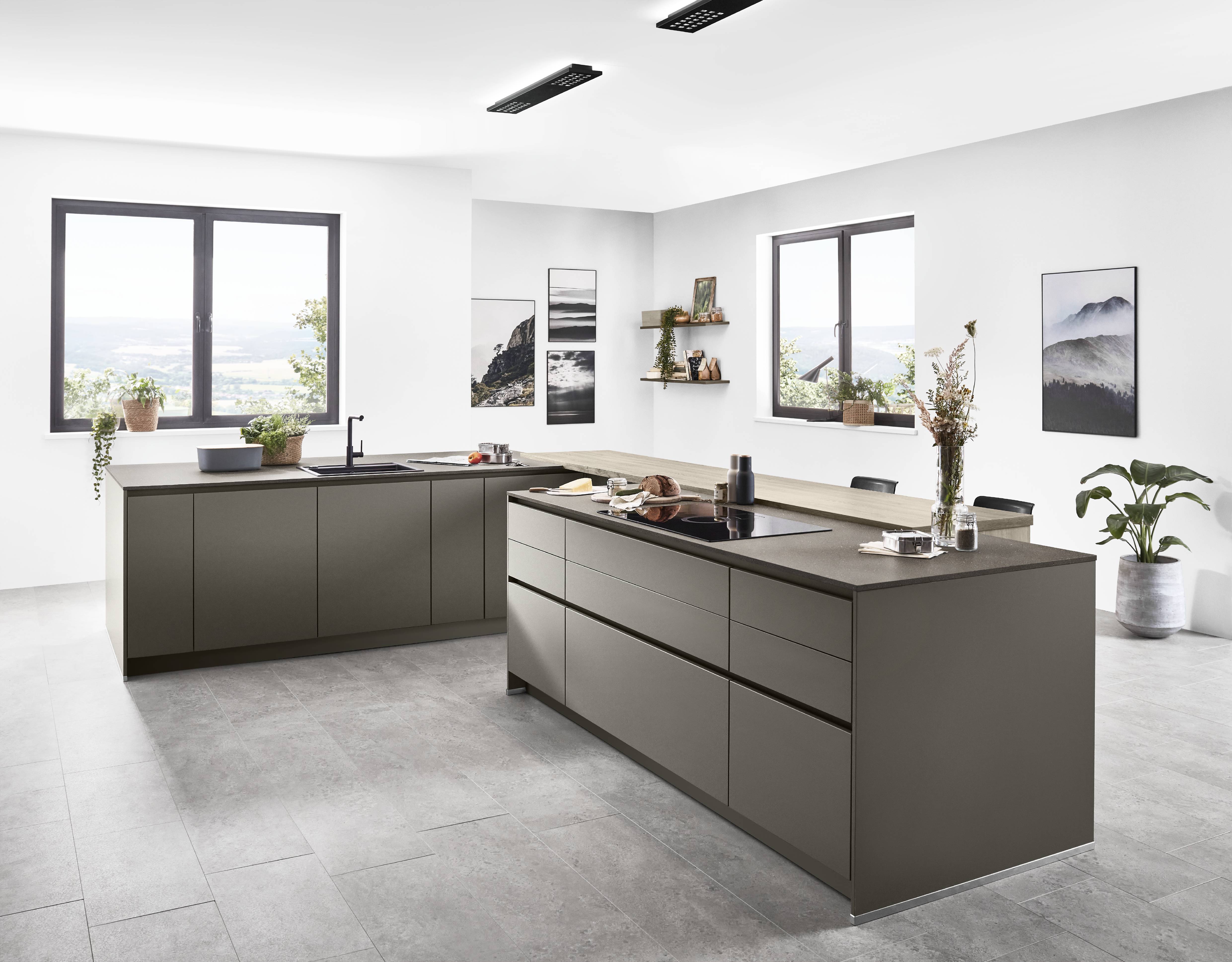 noblessa USA - Modern German Kitchen with Sleek Taupe Cabinetry and Spacious Island Modern German kitchen featuring streamlined taupe cabinetry, a large central island, integrated cooktop, open shelving, and expansive windows overlooking a scenic outdoor view.
