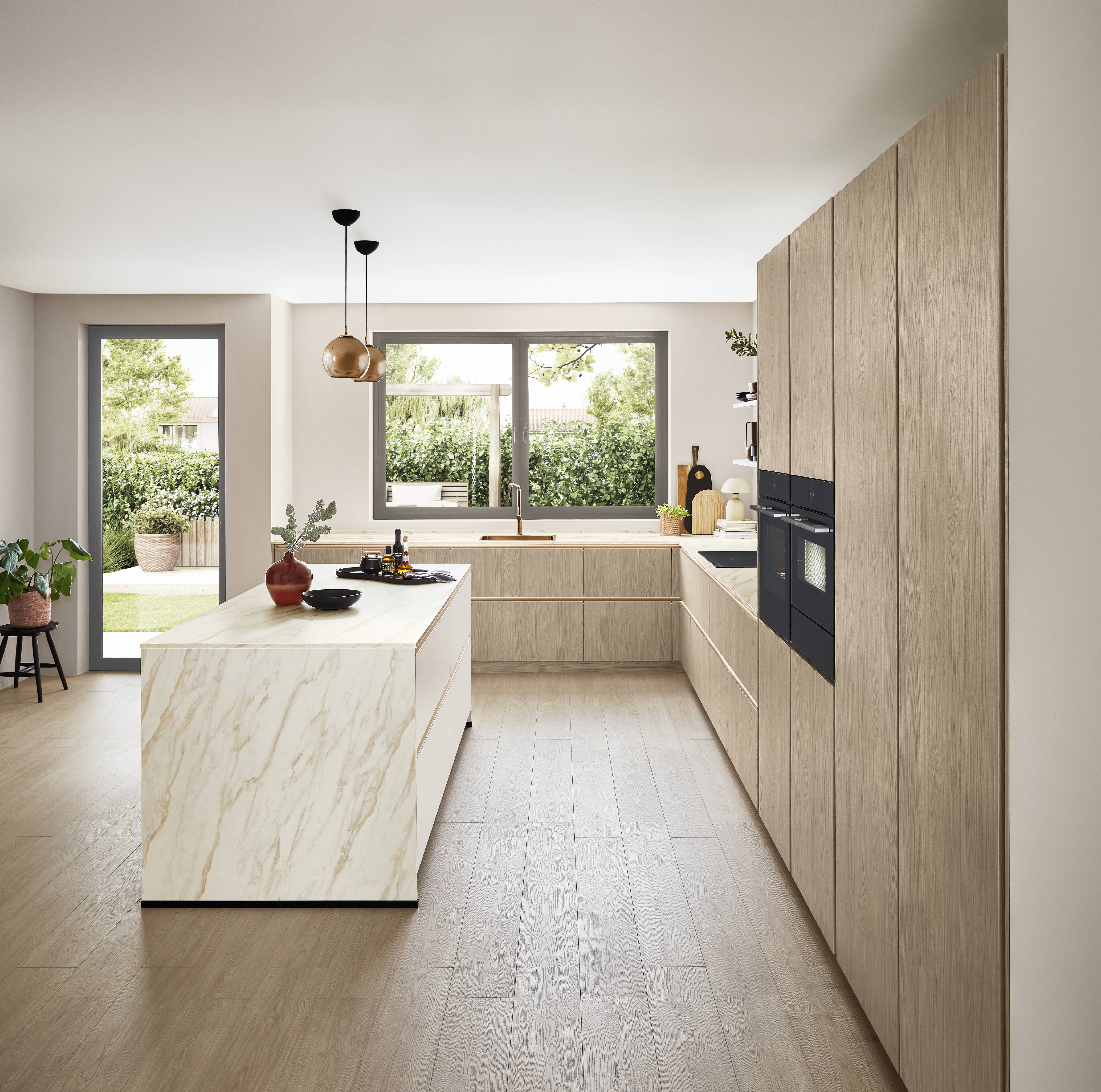 Modern German kitchen with light oak cabinetry, a marble-look waterfall island, integrated black appliances, and large windows that fill the minimalist space with natural light.