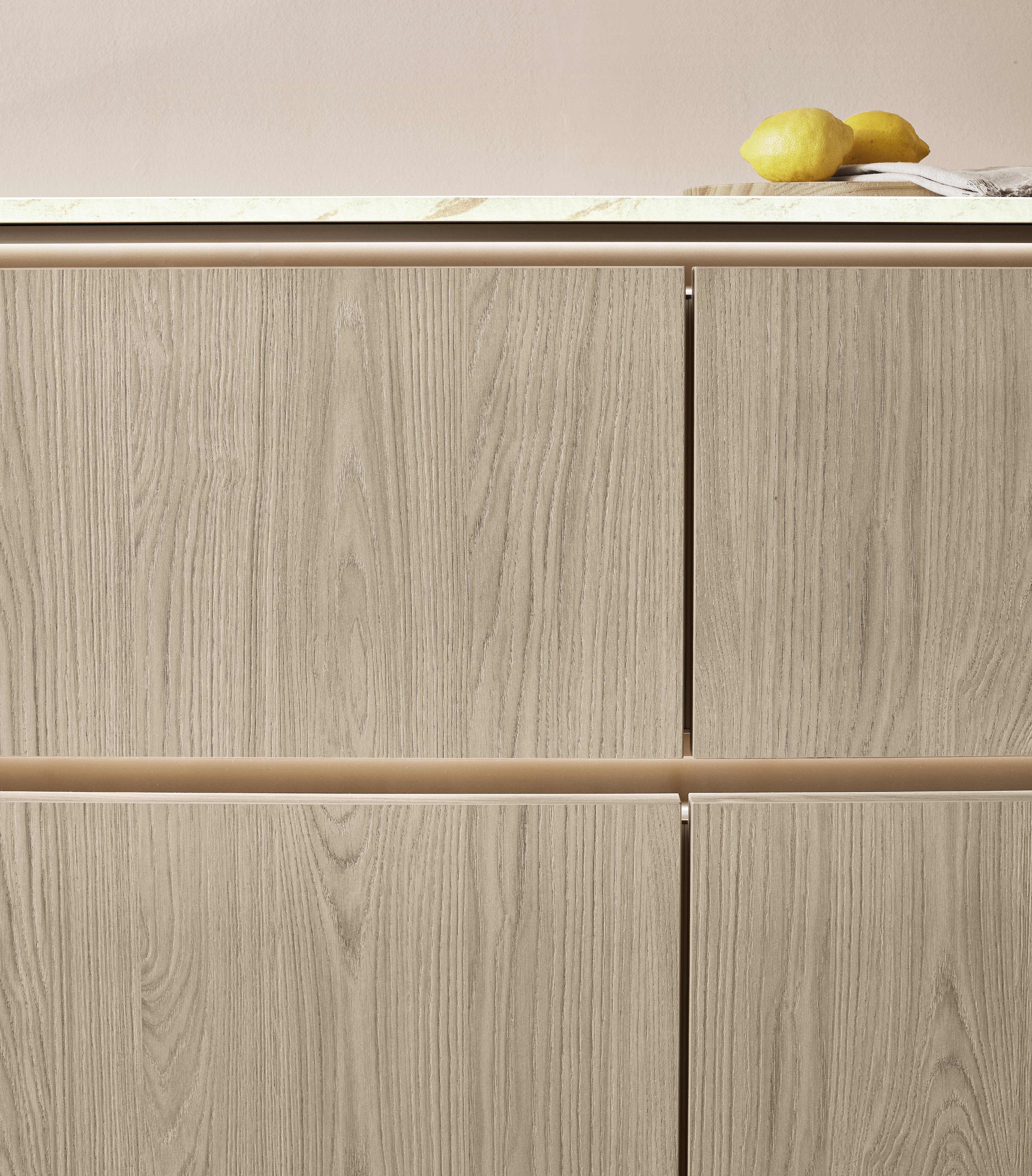 Close-up of light wood-look cabinet fronts with warm under-cabinet lighting and a stone countertop