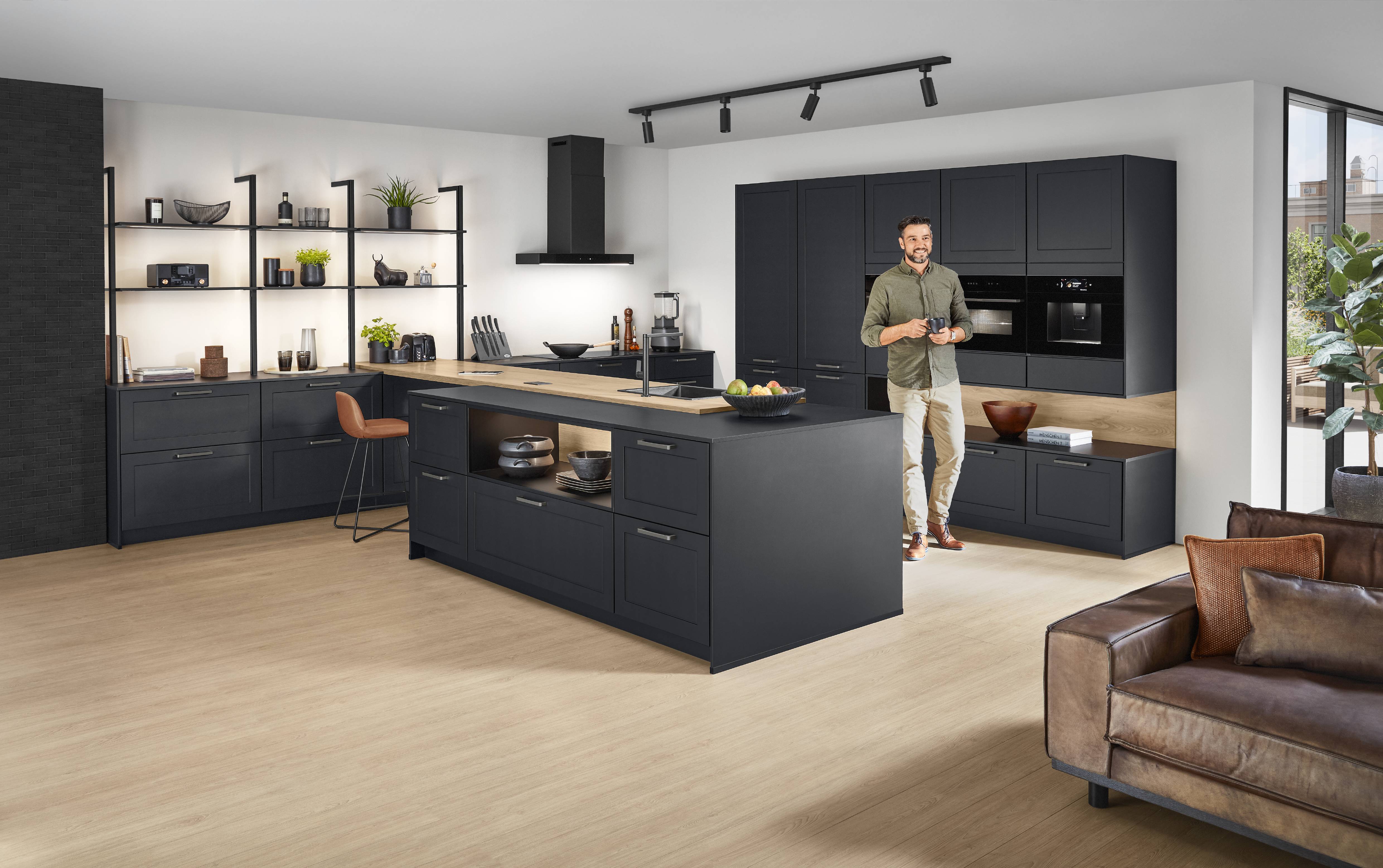 Open-plan kitchen with matte dark cabinetry, wood accents, open shelving, black track lighting, and a central island