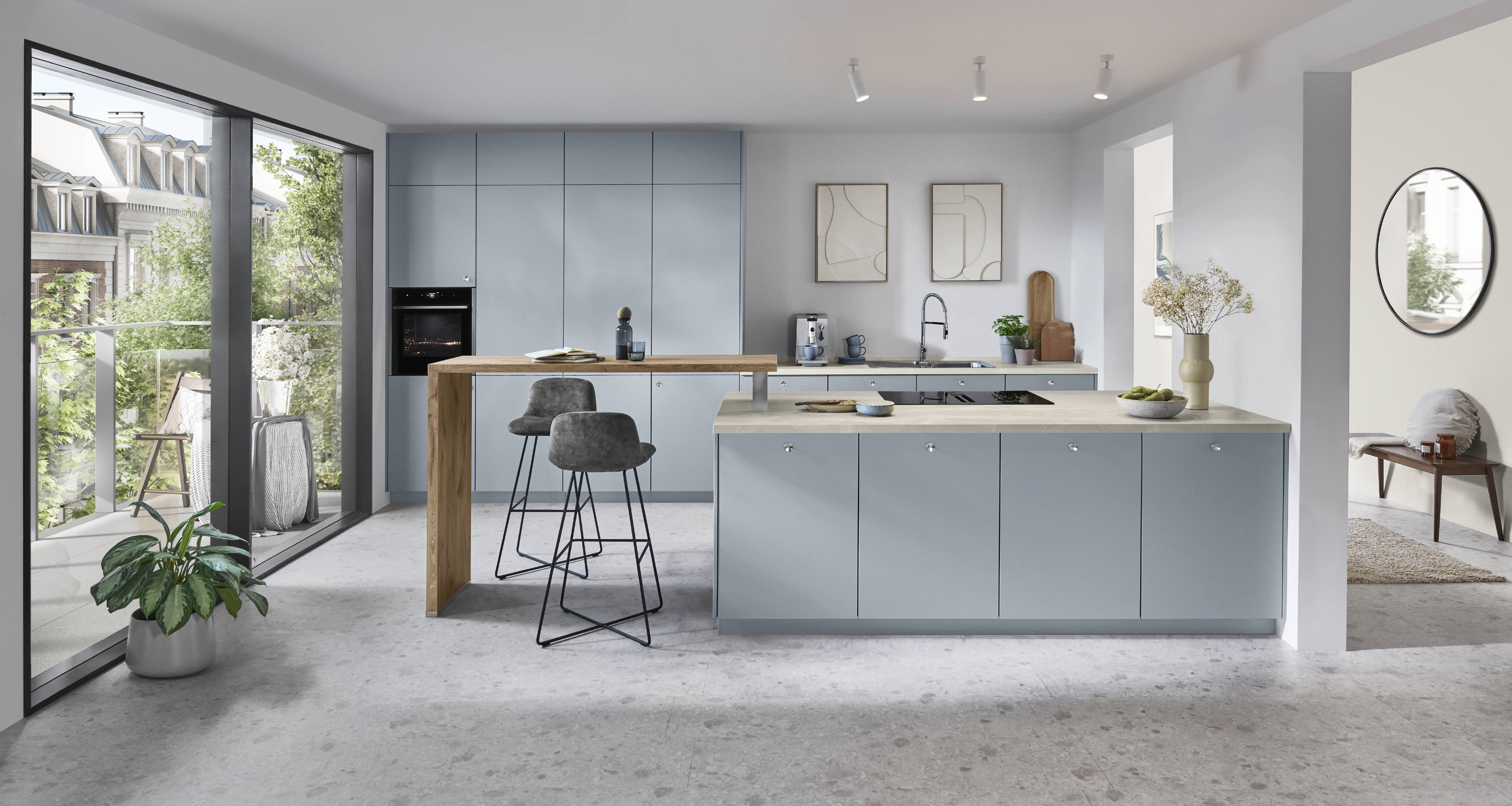 noblessa USA - Modern Blue-Gray German Kitchen with Open-Concept Dining Area Modern German kitchen featuring sleek blue-gray cabinetry, a large central island with a wood countertop, integrated double ovens, minimalist lighting, and an adjoining dining area with large windows.