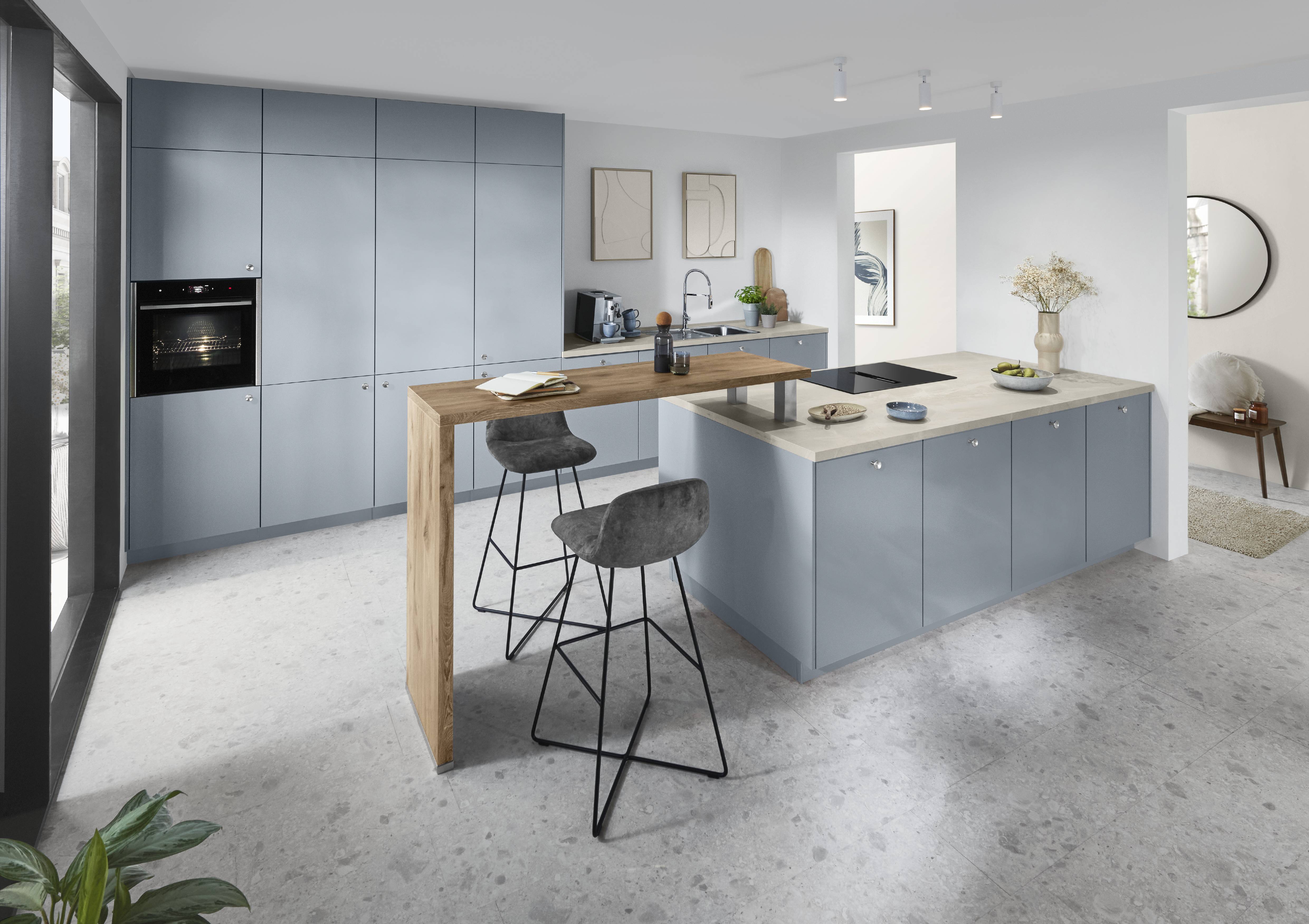 A sophisticated modern German kitchen featuring sleek blue-gray cabinetry, a spacious island with a light countertop, and a warm wood breakfast bar that adds contrast and inviting character to the space.