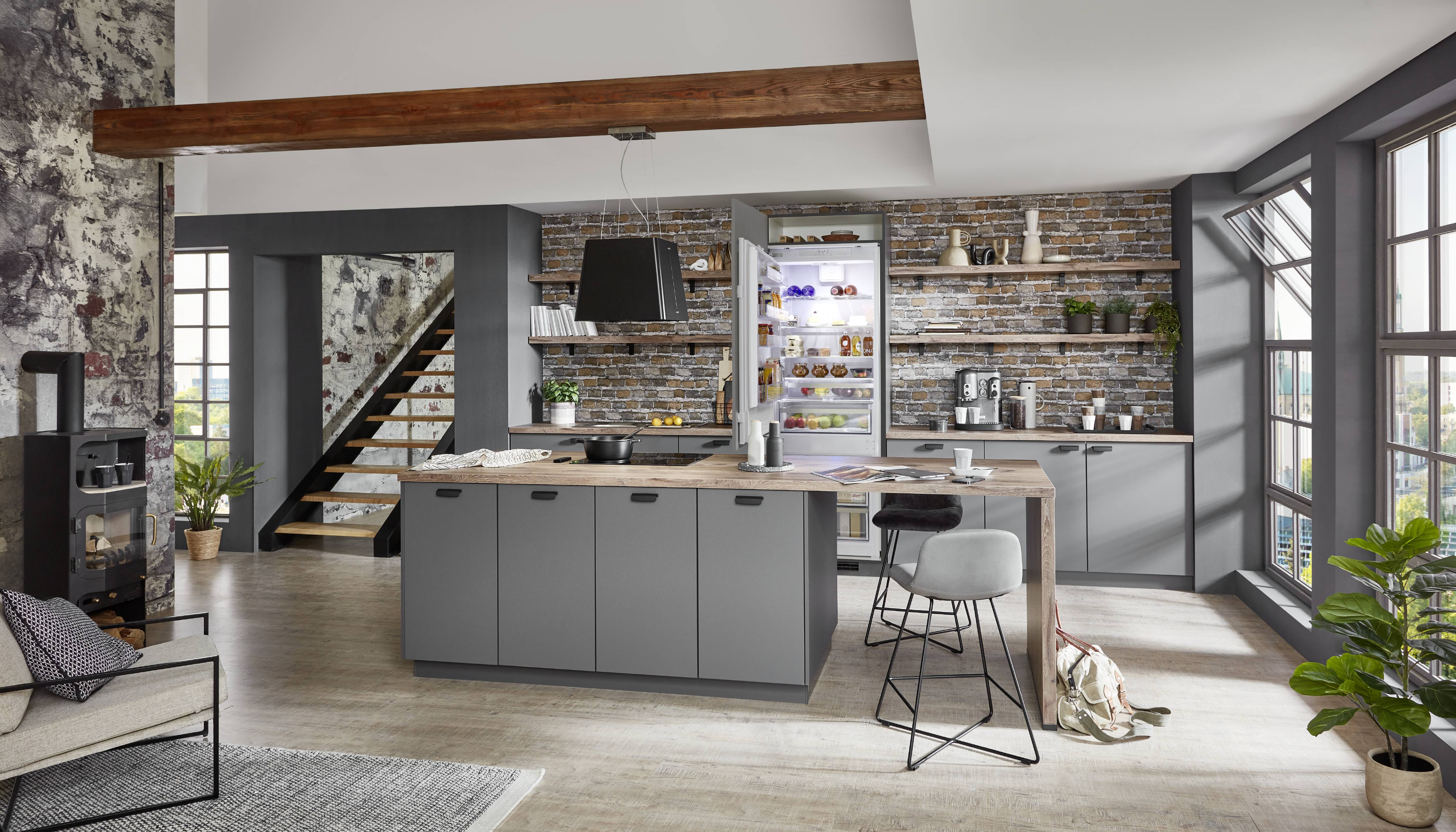 noblessa USA - Industrial German Kitchen with Charcoal Cabinetry, Wood Island, and Exposed Brick Accents Modern industrial-style German kitchen with matte charcoal cabinetry, a large wood-topped island, exposed brick walls, open shelving, integrated refrigerator, and floor-to-ceiling windows that flood the space with natural light.