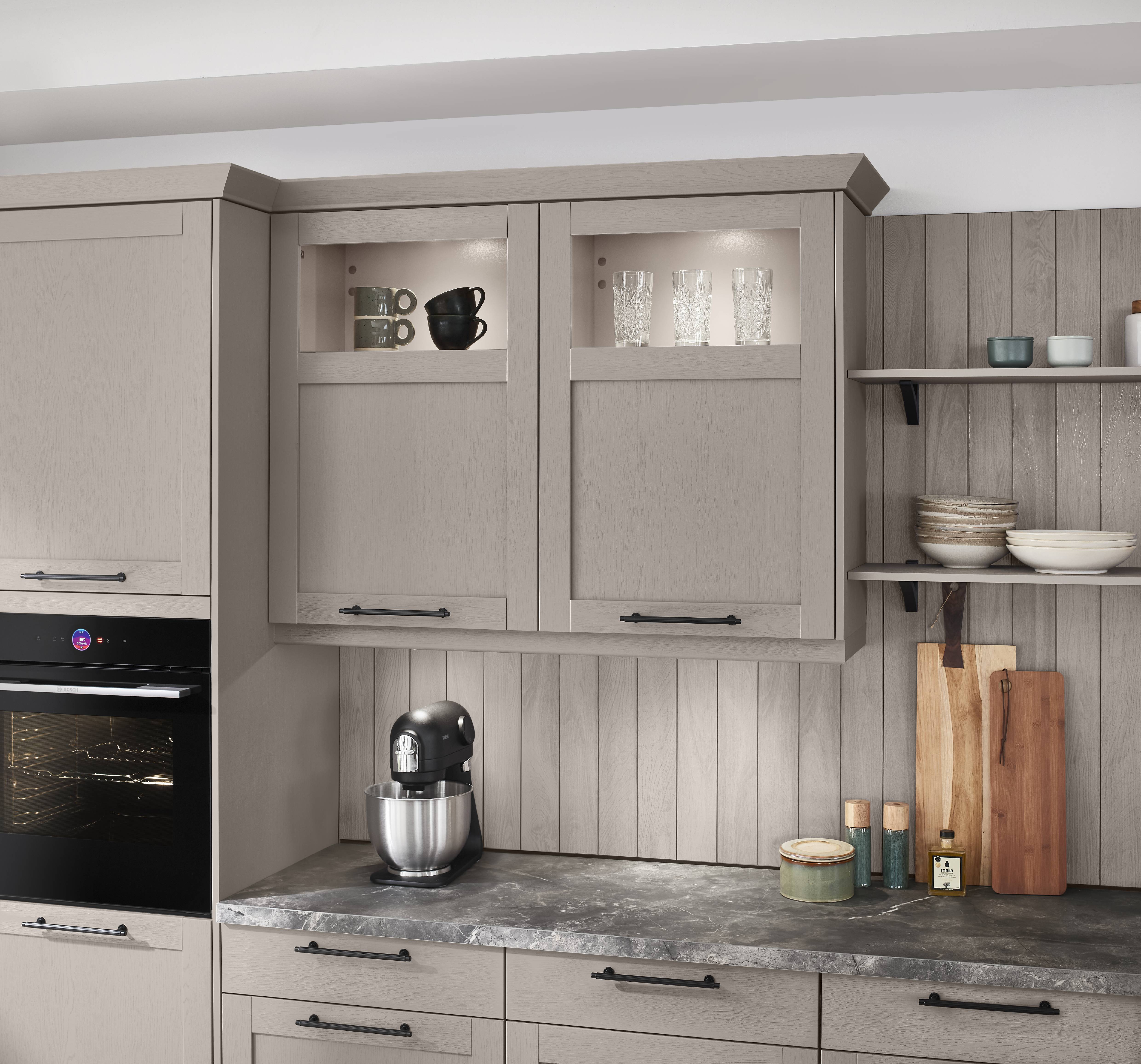 Close-up of a Noblessa USA German kitchen featuring taupe cabinetry, glass-front display cabinets, open shelving, dark stone countertops, and organized storage for kitchen essentials.