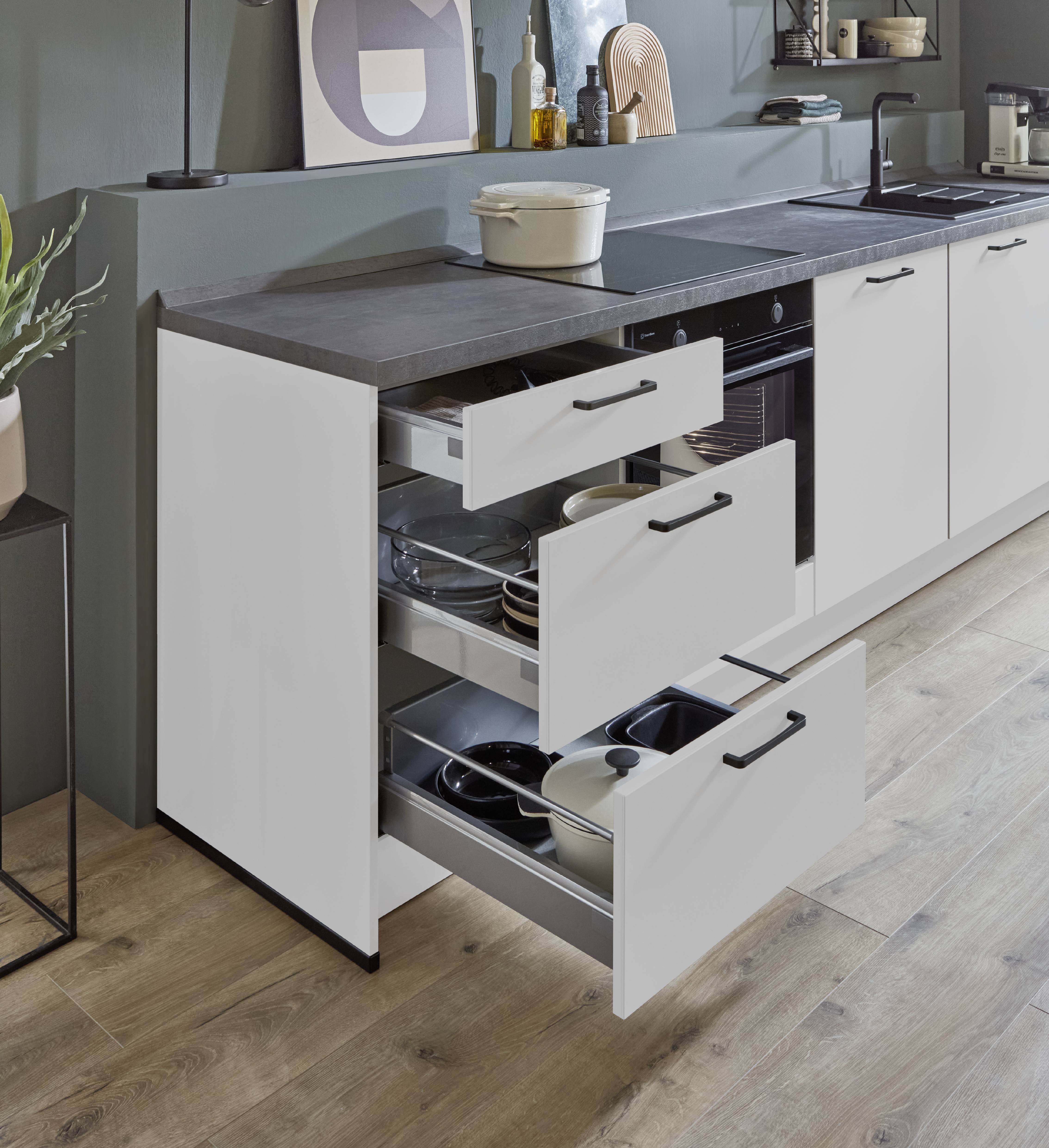 Modern white kitchen base cabinet featuring three pull-out storage drawers. The drawers are open and organized with cookware, dishes, and kitchen utensils, set beneath a gray countertop in a contemporary kitchen.