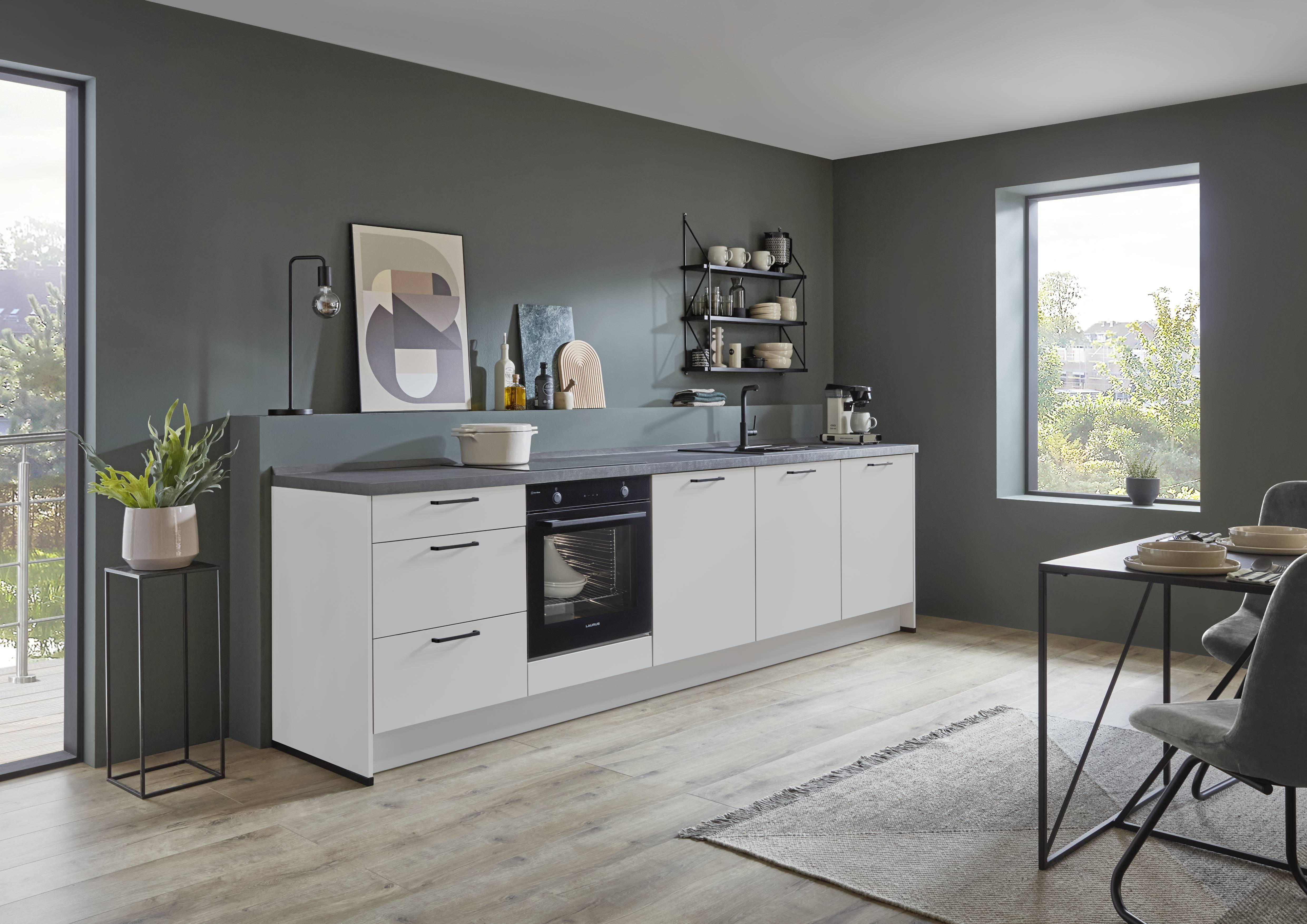 Modern German kitchen with matte white cabinets, integrated oven, dark accent walls, open shelving, wood flooring, and large windows that bring natural light into the space.