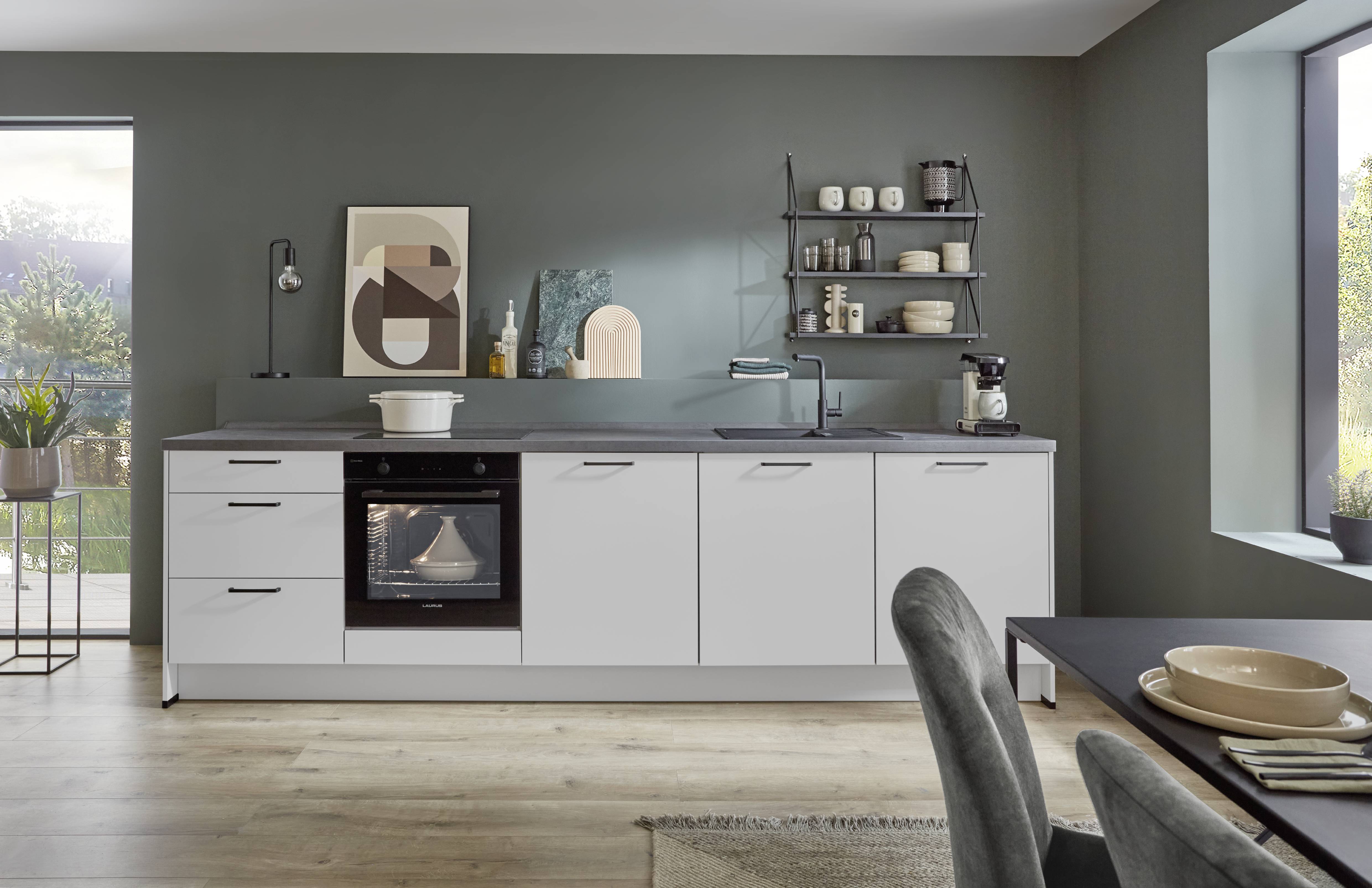 Modern kitchen featuring sleek white cabinets, a built-in black oven, gray countertop, and open wall shelving with dishes and décor. The space includes a matte gray backsplash, light wood flooring, and contemporary dining furniture, creating a clean and minimalist design.