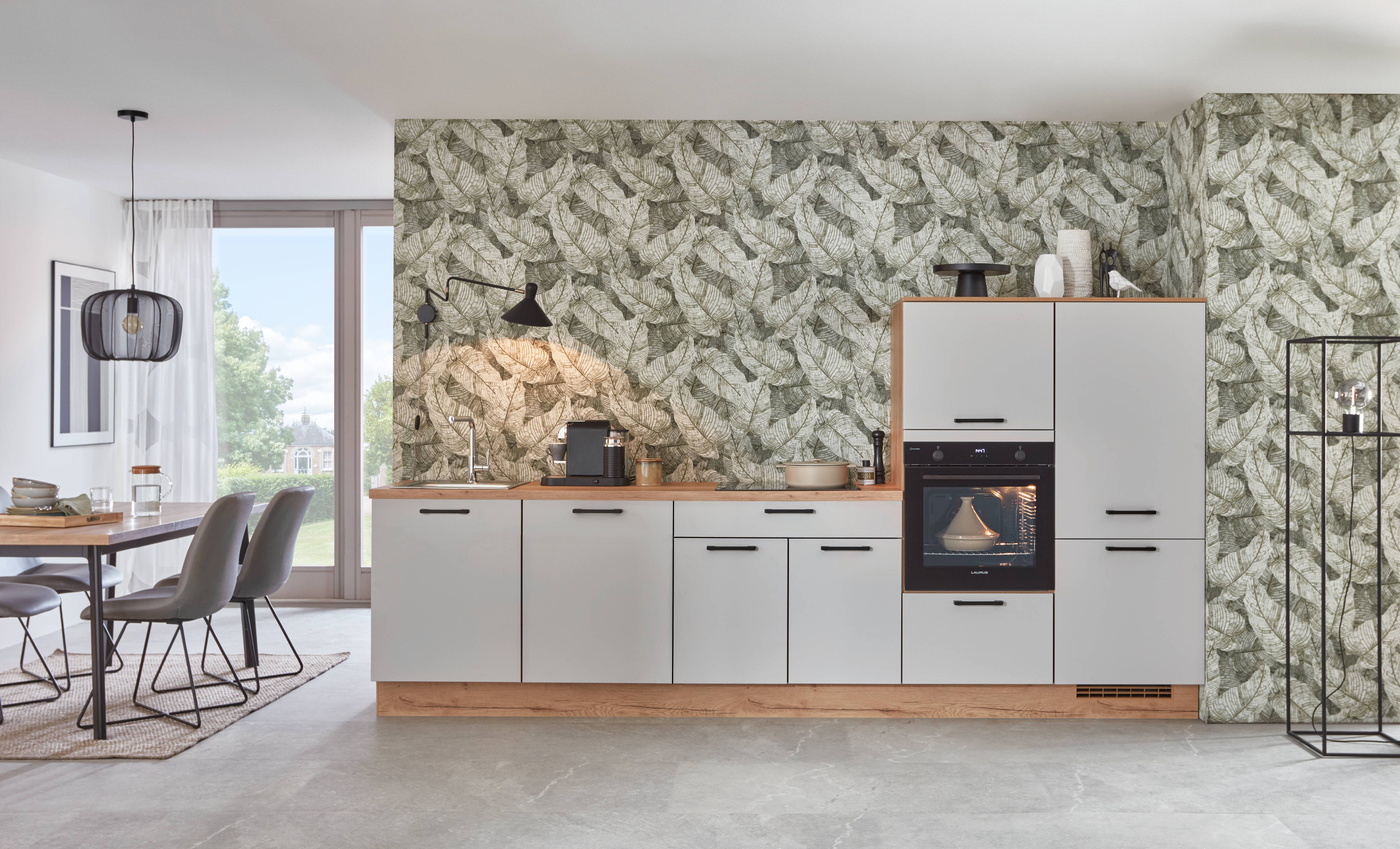 Noblessa USA - Modern German Kitchen with Botanical Accent Wall Modern German kitchen with matte white cabinetry, integrated oven, wood countertops, and botanical leaf-pattern wallpaper in an open-concept dining space.