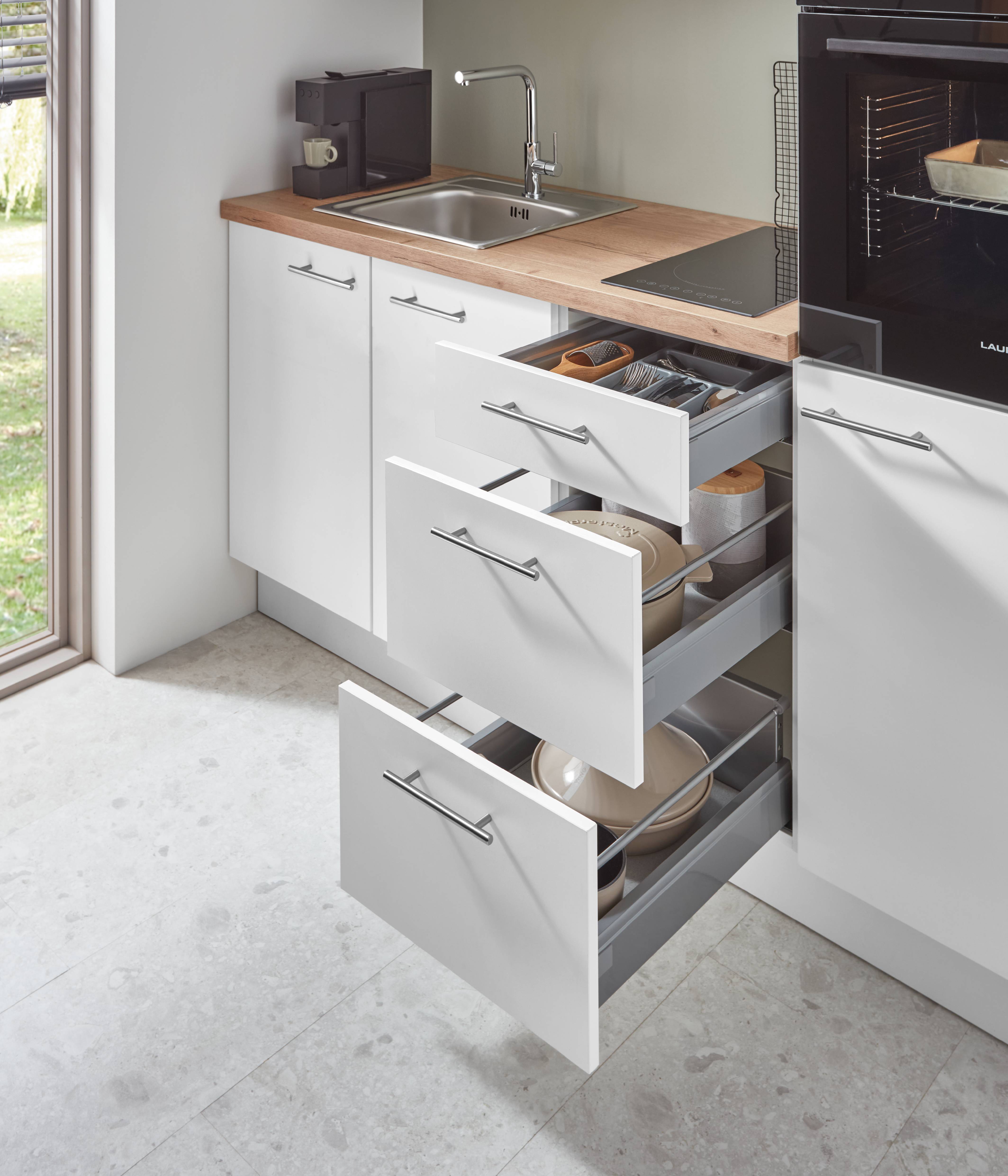 White kitchen drawer storage near sink and countertop workspace White kitchen drawers opened near a sink and countertop workspace, showing an organized, practical kitchen setup