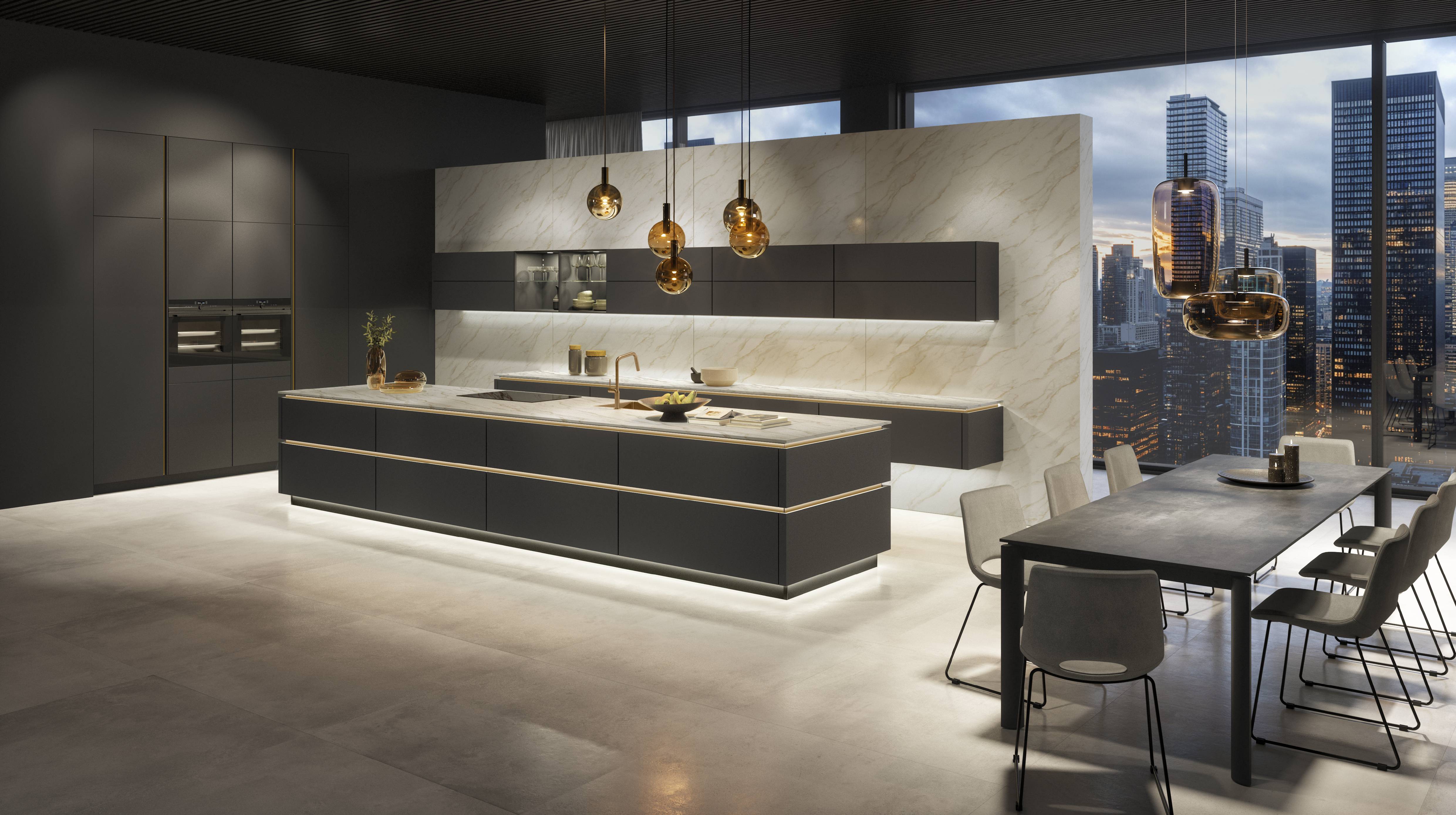 A sleek, modern Noblessa USA kitchen featuring a large matte black island with integrated lighting, marble backsplash and countertops, minimalist cabinetry, and warm pendant lights, set against floor-to-ceiling windows overlooking a city skyline at dusk.