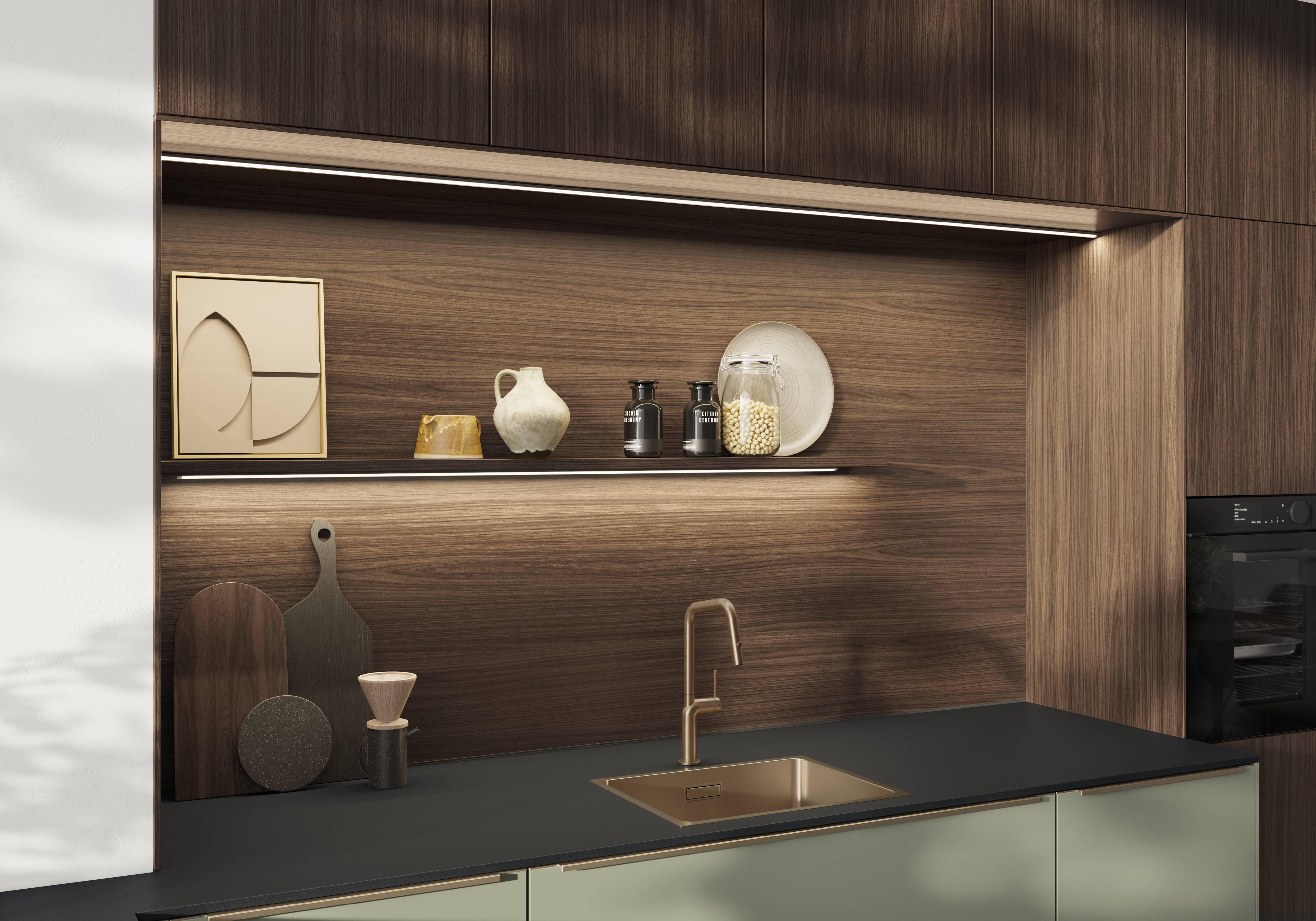 Walnut Wood European Kitchen with Integrated LED Shelving and Copper Fixtures - noblessa USA Close-up of a warm walnut wood European kitchen featuring LED-lit open shelving with decorative objects, a dark countertop, copper sink and faucet, and sage green lower cabinet fronts